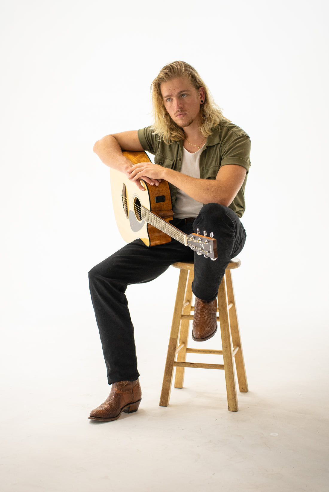 Stromer Hills sitting with guitar on stool